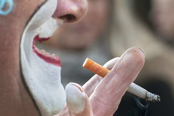 Un clown en train de regarder son maquillage dans un miroir pendant quil fume une cigarette à côté du Centre Pompidou.