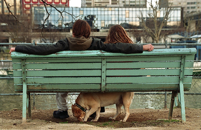 A young man and woman on a bench on allée des Cygnes with their dog.