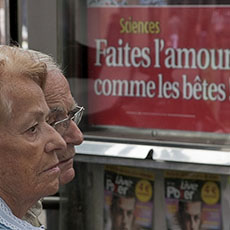 A couple in front of an advertisement for Marianne magazine with the headline «Faites l’amour comme les bêtes!», “Make love like animals”.