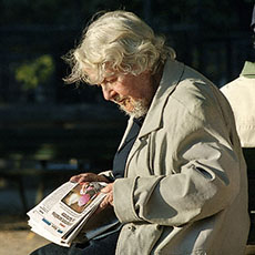 Une femme barbue en train de lire un journal derrière la cathédrale Notre-Dame.