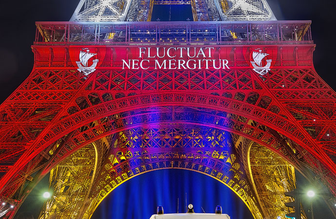 The Eiffel Tower with the city of Paris’ slogan, Fluctuat nec mergitur projected on it at night.