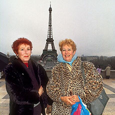 Two ladies, one wearing a leopard-skin coat, in front of the Eiffel Tower.