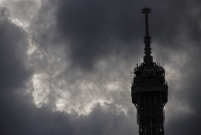 Grey clouds behind the top of the Eiffel Tower.