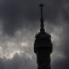 Grey clouds behind the top of the Eiffel Tower.