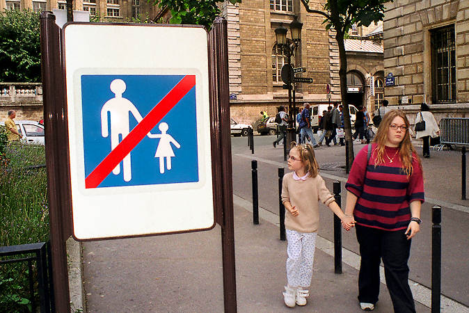 Two girls holding hands, walking past a sign indicating the end of a pedestrianized zone on île de la Cité.