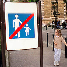 Two girls holding hands, walking past a sign indicating the end of a pedestrianized zone on île de la Cité.