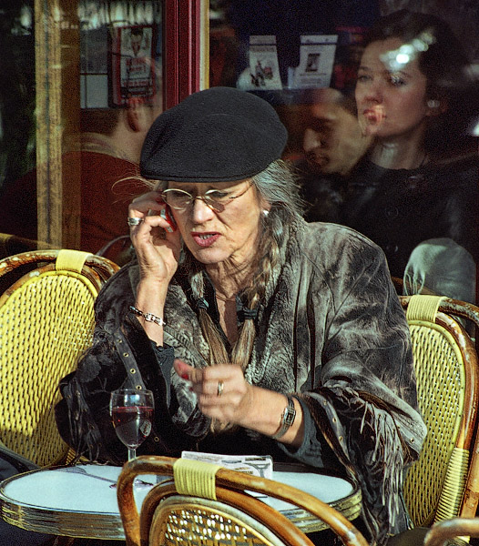 An older woman slamming her fist on a café table while talking on her cellphone on île Saint-Louis.