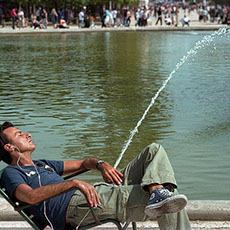 Un homme devant une fontaine du grand bassin rond dans le jardin des Tuileries en train d’écouter de la musique sur son iPod.