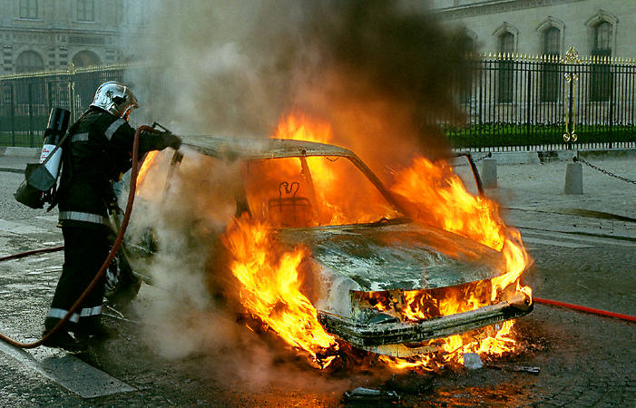 A car on fire next to the Louvre Museum.