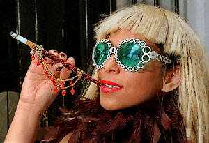 Lucy posing for portraits, with high-fashion sunglasses and a cigarette holder.