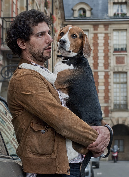 Un homme qui tient son chien dans ses bras dans la place des Vosges.