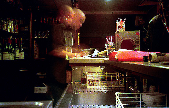 A barman in Café 6 on rue des Canettes at night.