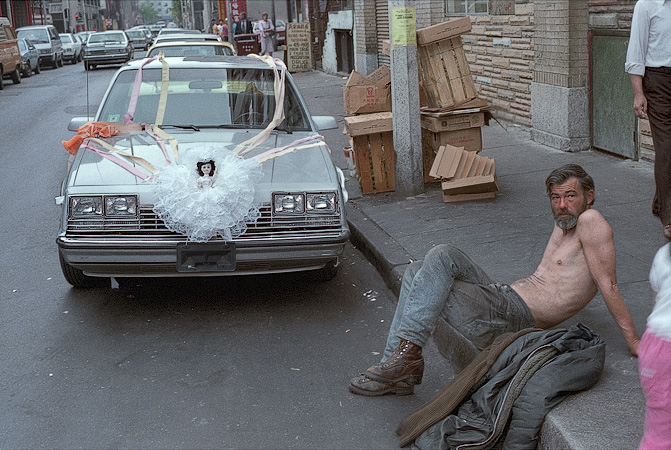 A homeless man sitting in front of a wedding car in Chinatown.