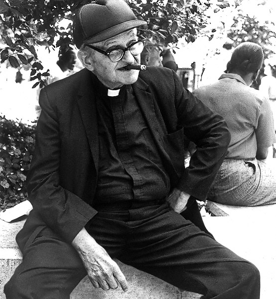A priest with a cigar, wearing a basball hat in Baltimore.
