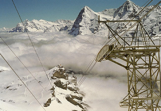 A view from above the clouds, looking down the slopes from a cable car