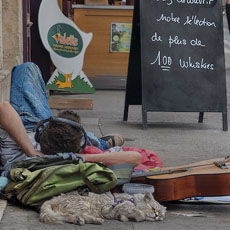 A young man dozing on the sidewalk in front of the Julien de Savignac liquor store with his sleeping bag, guitar and mangy cat on a leash.