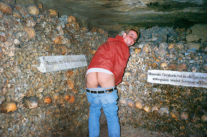 A young man mooning the bones and skeletons in the Catacombs of Paris.