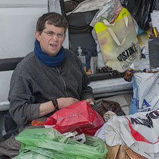 A homeless sitting in front of his van overflowing with trash, nonsense and junk.
