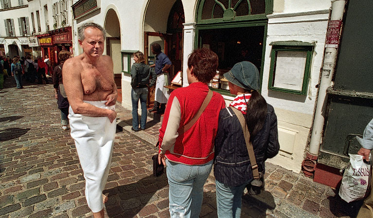 A man walking past place du Tertre wearing nothing but a bed sheet.