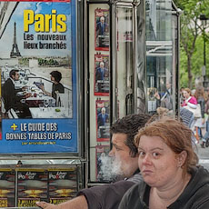 Three homeless people in front of a advertising poster for trendy spots and restaurants in Paris.